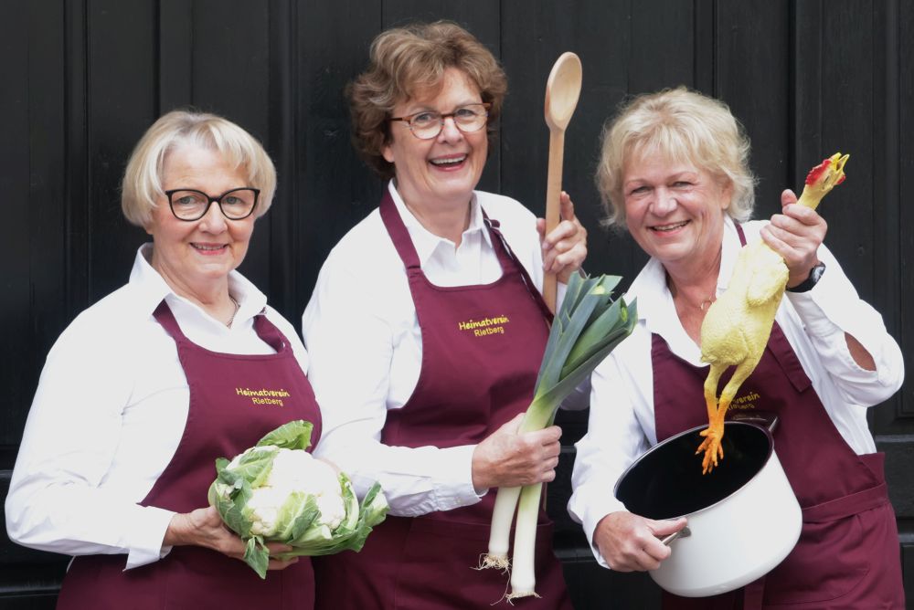 Die Gästeführerinnen Karin Hökenschnieder, Ute Merschbrock und Christa Honerlage mit Blumenkohl, Kochlöffel, Topf und Hühnchen.